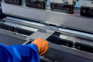 Worker using a steel press break, bending a sheet metal part