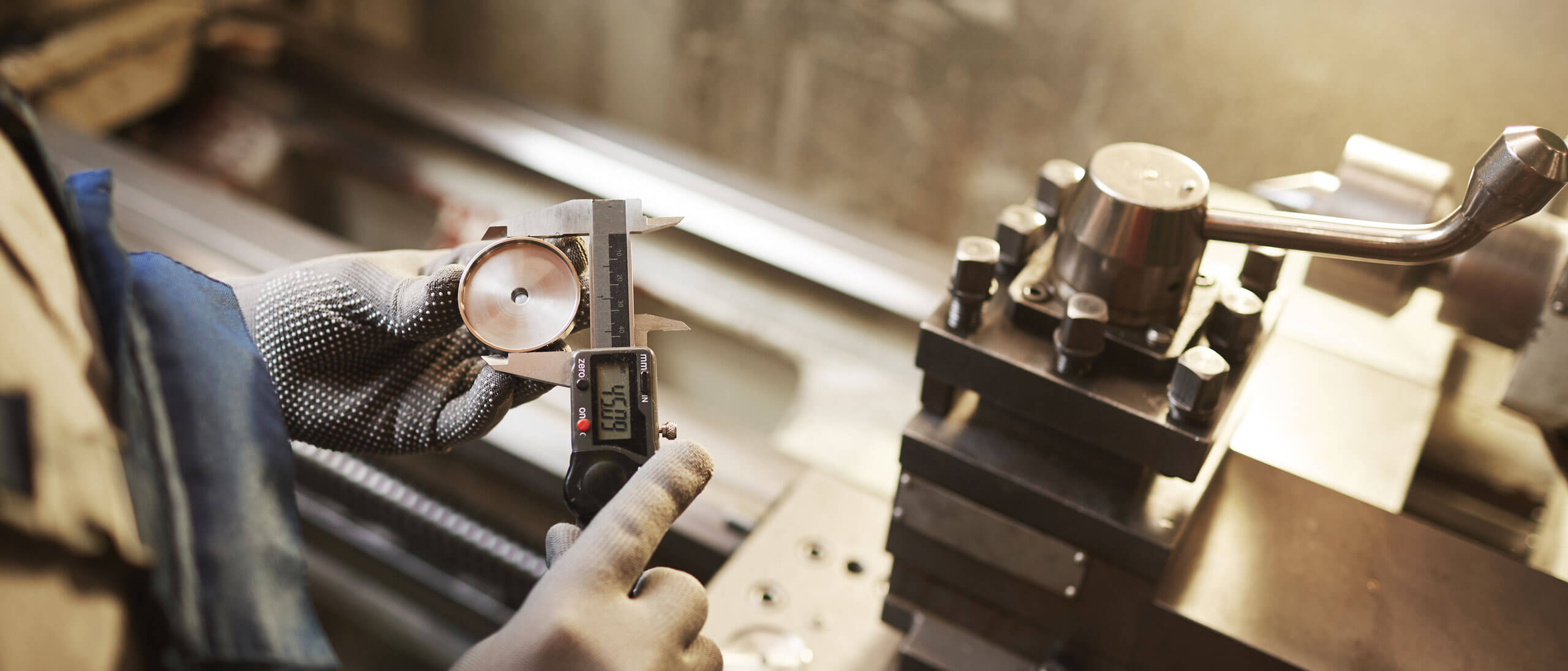 Toolmaker using calipers to measure a machined steel part